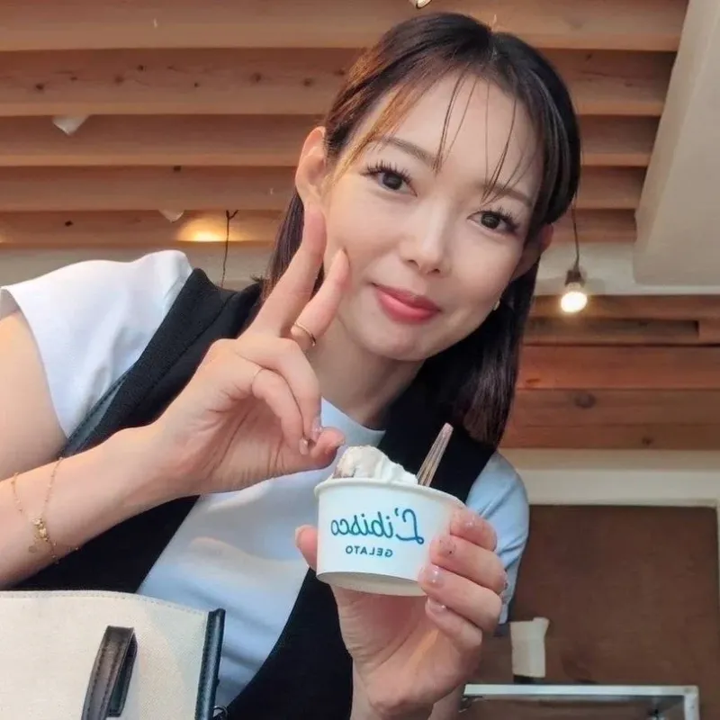 カフェのような場所で、笑顔の女性がジェラートのカップを持ち、ピースサインをしています。楽しそうでリラックスした雰囲気が伝わってきます。
