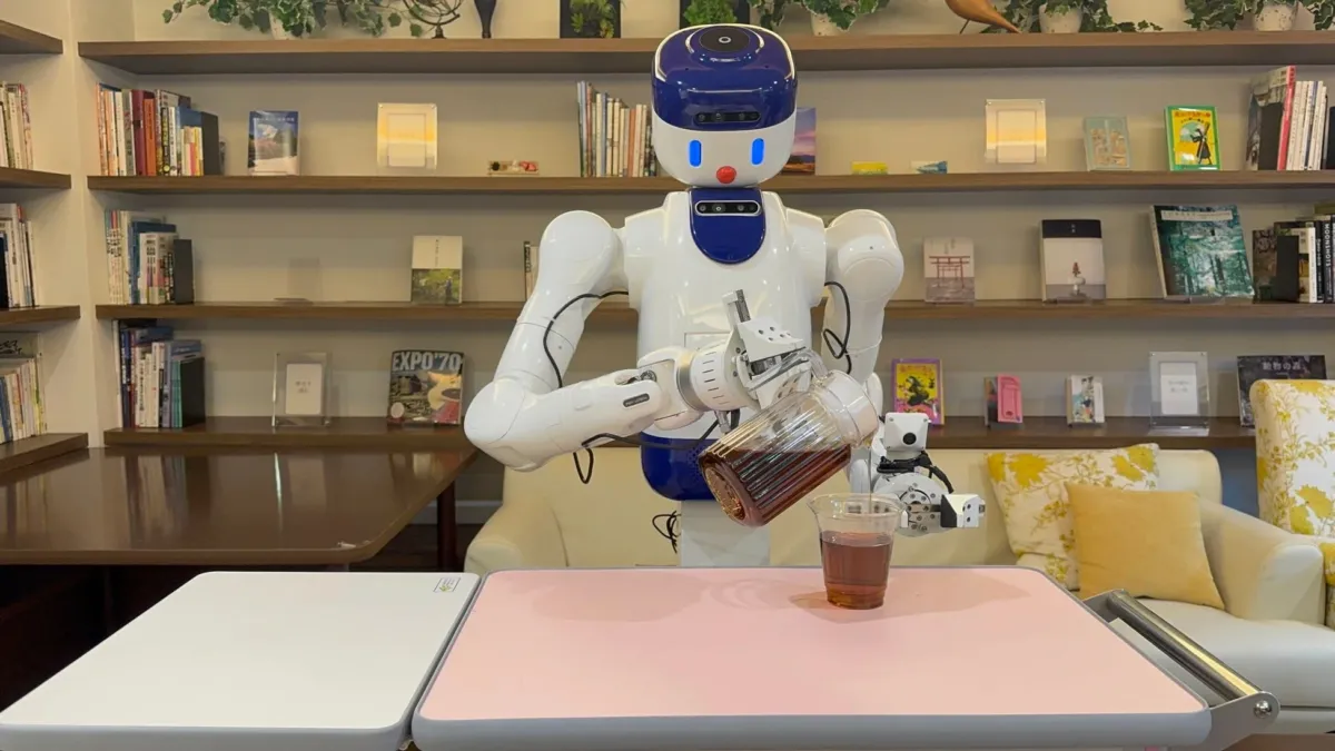 書棚のある落ち着いた空間で、人型ロボットがカップに飲み物を注いでいる様子。未来のカフェやサービス業におけるロボットの活用を示唆している。